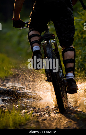 A mountain biker riding though a sunlit puddle on Idaho Peak in New Denver, British Columbia, Canada Stock Photo