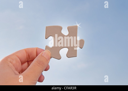 Hand holding a jigsaw piece against the sun Stock Photo