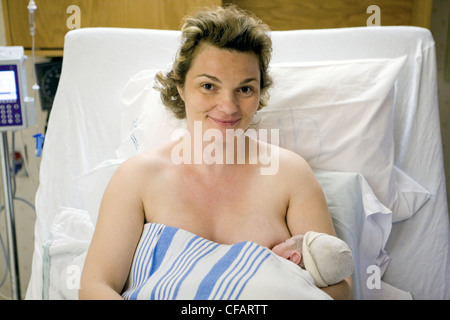 36 year old woman lying in hospital bed breastfeeding her newborn, Chateauguay, Quebec, Canada Stock Photo