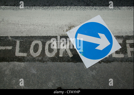 A blue sign on the road surface covering a 'look left' instruction painted on the road, London. Stock Photo