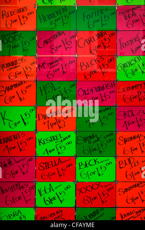 Window full of brightly coloured, fluorescent signs advertising deals on lagers and beers in window of London shop Stock Photo