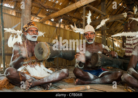 Men from the Asmat Tribe playing drums and singing, Agats village, New Guinea, Indonesia. Stock Photo