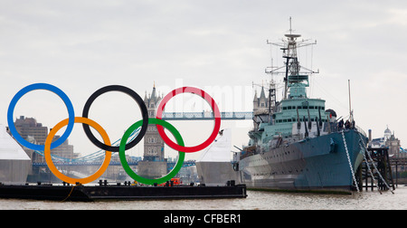 Large Olympic rings, 11m high by 25m wide are floated down the River Thames on a barge in front of Tower Bridge and HMS Belfast