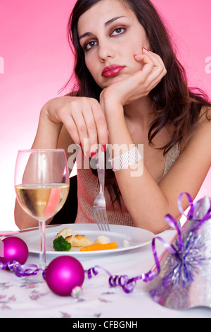 Female long brunette hair diamante hairclip wearing gold halterneck top sitting at table in front of plate small pieces of Stock Photo