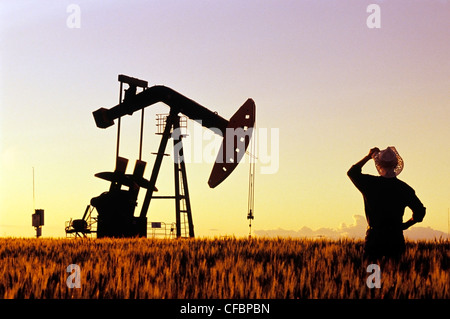 A farmer looks out over a maturing wheat crop with an oil pumpjack in the background near Carlyle, Saskatchewan, Canada