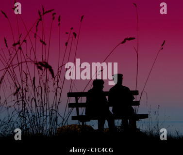 An elderly couple in silhouette profile on a park bench. Stock Photo