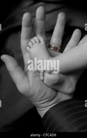 Black and white of newborn's feet on the hand of father with wedding ring. Stock Photo