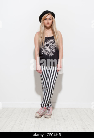 Full length colour studio portrait of female on white background wearing black and white jeans and black bowler hat legs crossed Stock Photo