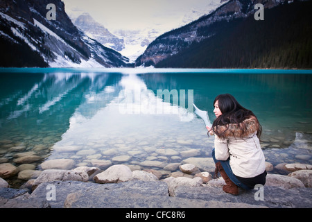 Young teenage girl tourist, holding up piece of ice from Lake Louise. Banff National Park, Alberta, Canada. Stock Photo