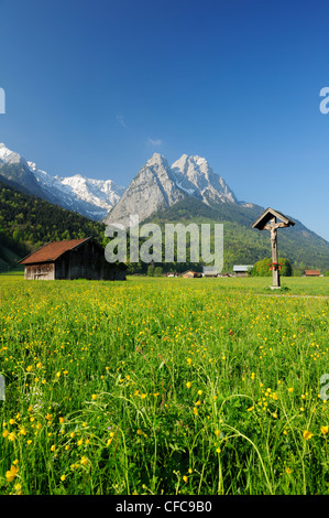 Meadow with flowers, hay sheds and wayside cross in front of Zugspitze range with Waxenstein, Garmisch-Partenkirchen, Wetterstei Stock Photo