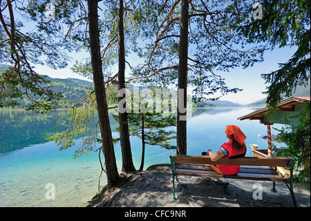Woman sitting on wooden bench and enjoying view of lake Weissensee, lake Weissensee, Carinthia, Austria, Europe Stock Photo