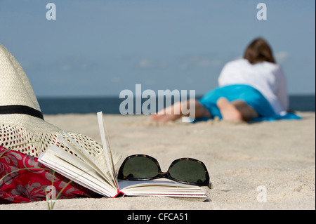 Woman lying at beach, book and sunglasses in foreground, List, Sylt, Schleswig-Holstein, Germany Stock Photo