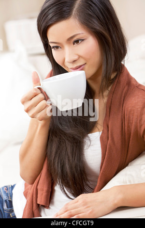 A beautiful young Chinese Asian Oriental woman with a wonderful toothy smile drinking tea or coffee from a white cup and saucer Stock Photo