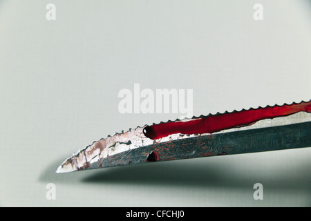 A simulated serrated edged bloodied knife with focus on the centre left drop of 'blood'. Stock Photo