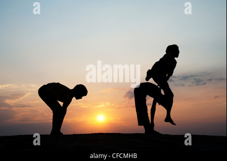 Silhouette of young Indian boys playing leap frog against at sunset. India