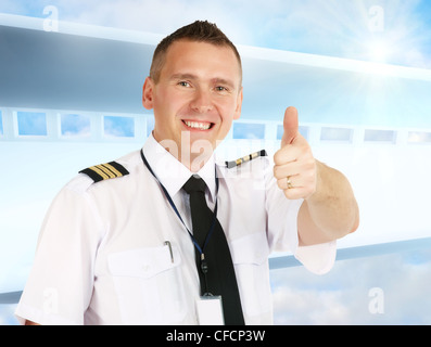 Cheerful airline pilot wearing uniform with epauletes showing thumb up gesture of approval, standing over modern background. Stock Photo