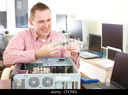 Repairman working with computer with a part in hands. Monitors and other laptops in the background waiting for service. Stock Photo