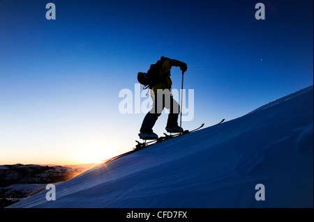 A silhouette of a skier skinning up a snow covered slope at sunrise in the Sierra Nevada near Lake Tahoe, California. Stock Photo