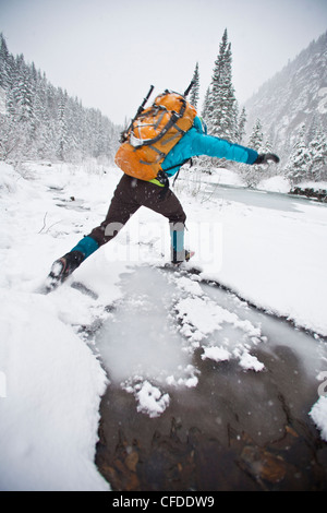 A woman puddle jumping on her way to ice climb Moonlight WI4, Even Thomas Creek, Kananaskis, Alberta, Canada Stock Photo