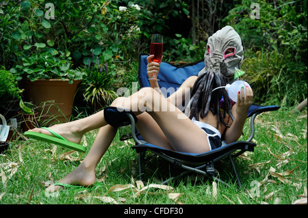 10 year old child dressed in home-made Ood mask, relaxing outdoors in sun with a drink. Stock Photo