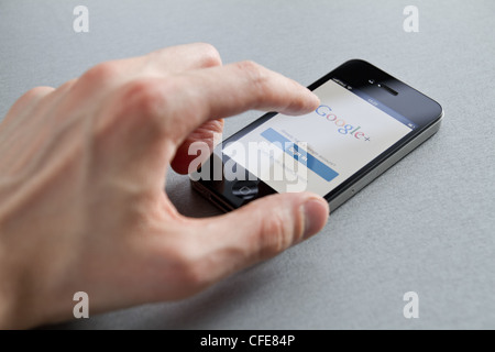 Man hand touching Apple iPhone with Google+ page on screen. Google+ is a social network service created by Google inc. Stock Photo