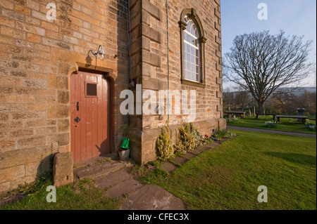 External doorway entrance (wooden door closed) at base of church tower & churchyard gravestones - St Peter's Church, Addingham, West Yorkshire, GB, UK. Stock Photo