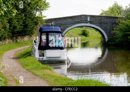 Pleasure cruiser (boat) moored in scenic rural area by small stone bridge on banks of Leeds Liverpool Canal - Gargrave, North Yorkshire, England, UK. Stock Photo