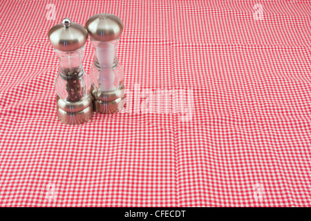 Salt and pepper shakers on red and white gingham tablecloth. Stock Photo