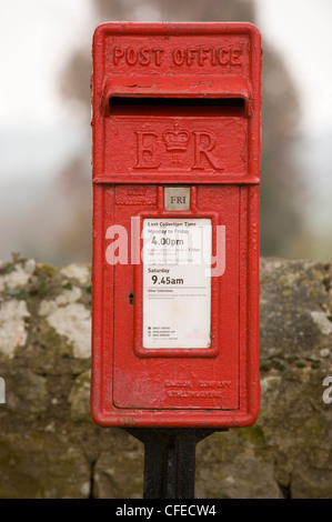 Close-up front view of bright red post box (lamp box style, marked ER) standing in front of drystone wall - Leathley, North Yorkshire, England, UK. Stock Photo