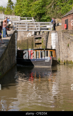 Sunny boat trip (people stand, watching as narrowboat steers out of bottom lock chamber) - Five Rise Locks, Bingley, Leeds Liverpool Canal, England. Stock Photo