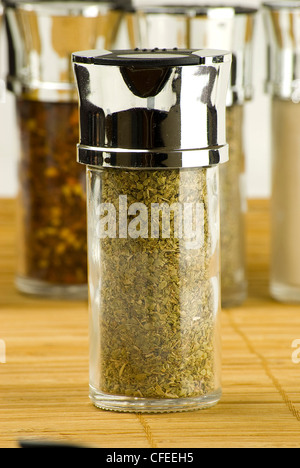 oregano in a glass jar on different spices background over wooden mat Stock Photo