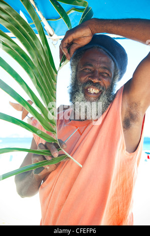Bearded Smiling Local Rastafarian black man wearing hat holding palm frond, Orient Beach, Saint Martin Stock Photo