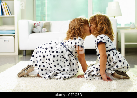 Portrait of happy twin girls kissing at home Stock Photo