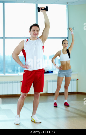 Image of young man doing exercise with barbells with pretty girl on background Stock Photo