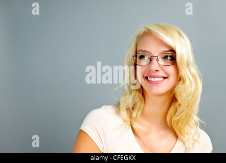 Smiling young woman wearing glasses looking to the side on grey background Stock Photo