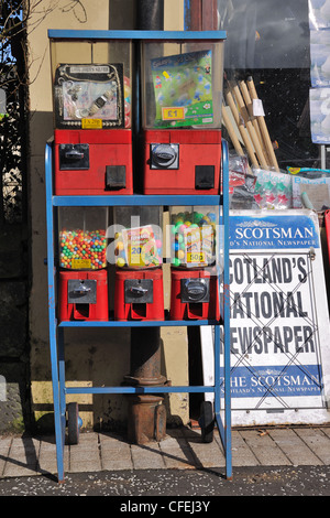Retro styled coin operated sweet dispenser and newspaper advertisement outside of a newsagent in Barrhead, Scotland, UK