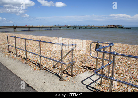 Deal pier in Kent viewed through the chrome safety rails on the promenade, across the pebble beach Stock Photo