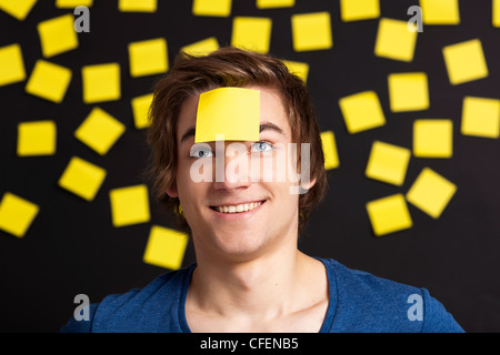 Happy student with a reminder on the head, and with more yellow paper notes in the background Stock Photo