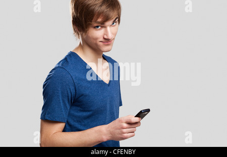 Portrait of handsome young man sending text messages with is mobile phone, over a gray background Stock Photo