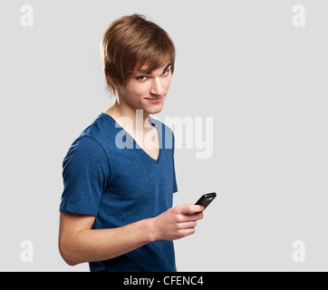 Portrait of handsome young man sending text messages with is mobile phone, over a gray background Stock Photo