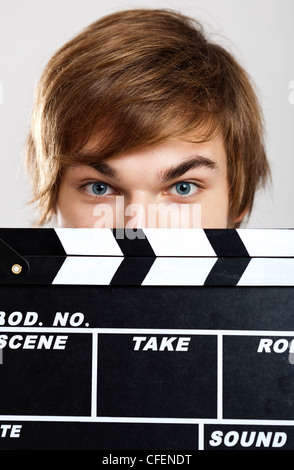 Portrait of a young man peeking behind a clapboard, over a gray background Stock Photo