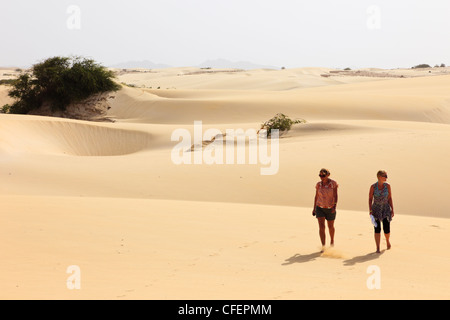 View of two women tourists walking barefoot on hot empty desert sand dunes. Deserto de Viana, Boa Vista, Cape Verde Islands. Stock Photo