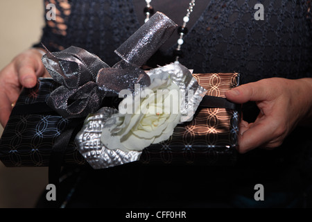 Female hands holding a present decorated with a bow and flower Stock Photo