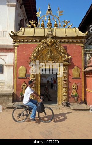 Man cycling past the Golden Gate, Sun Dhoka, in Durbar Square, Bhaktapur, UNESCO World Heritage Site, Kathmandu Valley, Nepal Stock Photo