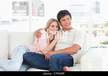 Woman and man holding each other on the couch, smiling and looking to the side Stock Photo