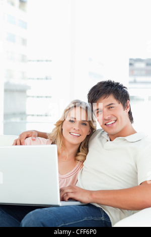 Man and woman looking straight ahead as they use the laptop on the couch Stock Photo