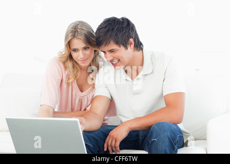 Smiling man and woman using the laptop as they sit on the couch together Stock Photo
