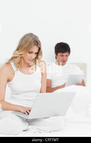 Woman using laptop while man uses the tablet on the bed Stock Photo
