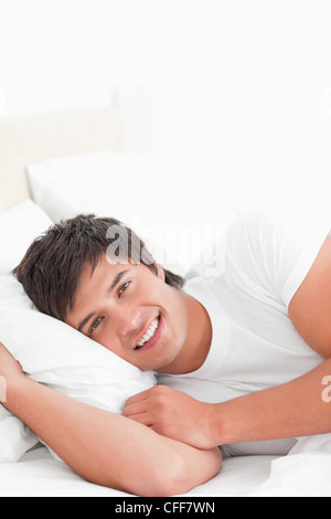 Close up, man lying on bed looking forward with his head on the pillow smiling Stock Photo