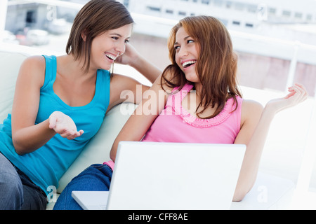 Two friends sitting on a sofa while talking about the laptop Stock Photo